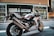 A sleek Honda motorcycle is parked on an urban street. The design of the motorcycle features a sporty build with a color scheme of white, red, and blue. It is positioned in front of a modern building with large windows and decorative patterns.