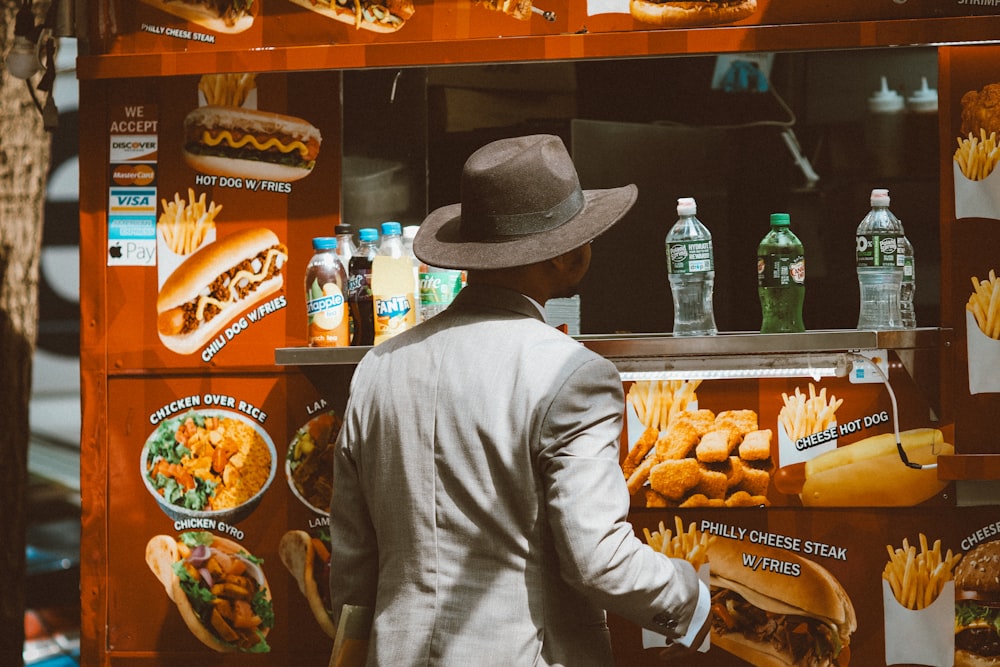 a man in a hat standing in front of a hot dog stand