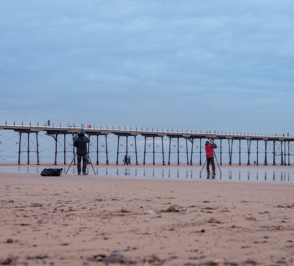 a couple of people standing on top of a sandy beach