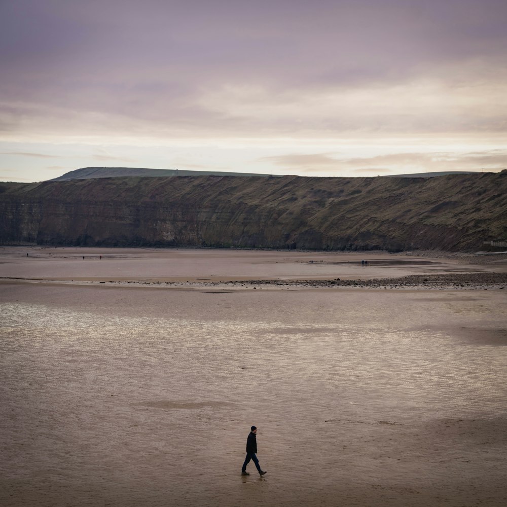 a person walking on a beach near a hill