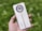A hand is holding a sleek white smartphone with a circular camera module. The phone has a light orange vertical strip running through the center. The brand name 'realme' is visible on its back. The background is blurred, consisting of lush green foliage.