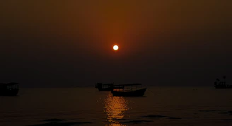 A serene sunset over the Mandovi River with silhouetted boats drifting gently.