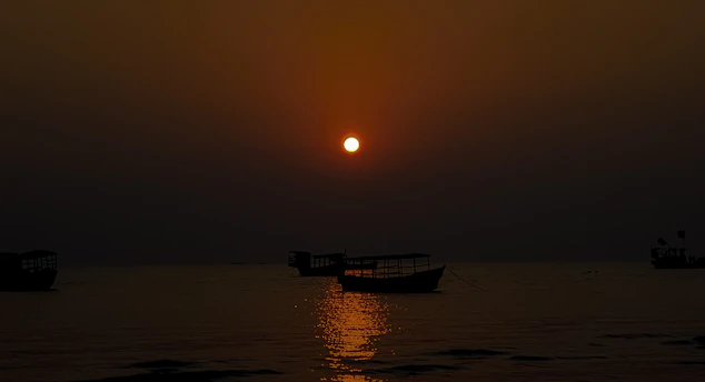 A serene sunset over the Mandovi River with silhouetted boats drifting gently.