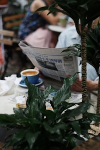A diverse group of people reading newspapers in a modern café setting.
