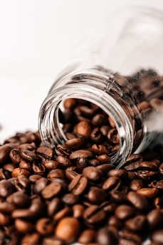 a glass jar filled with coffee beans sitting on top of a pile of coffee beans