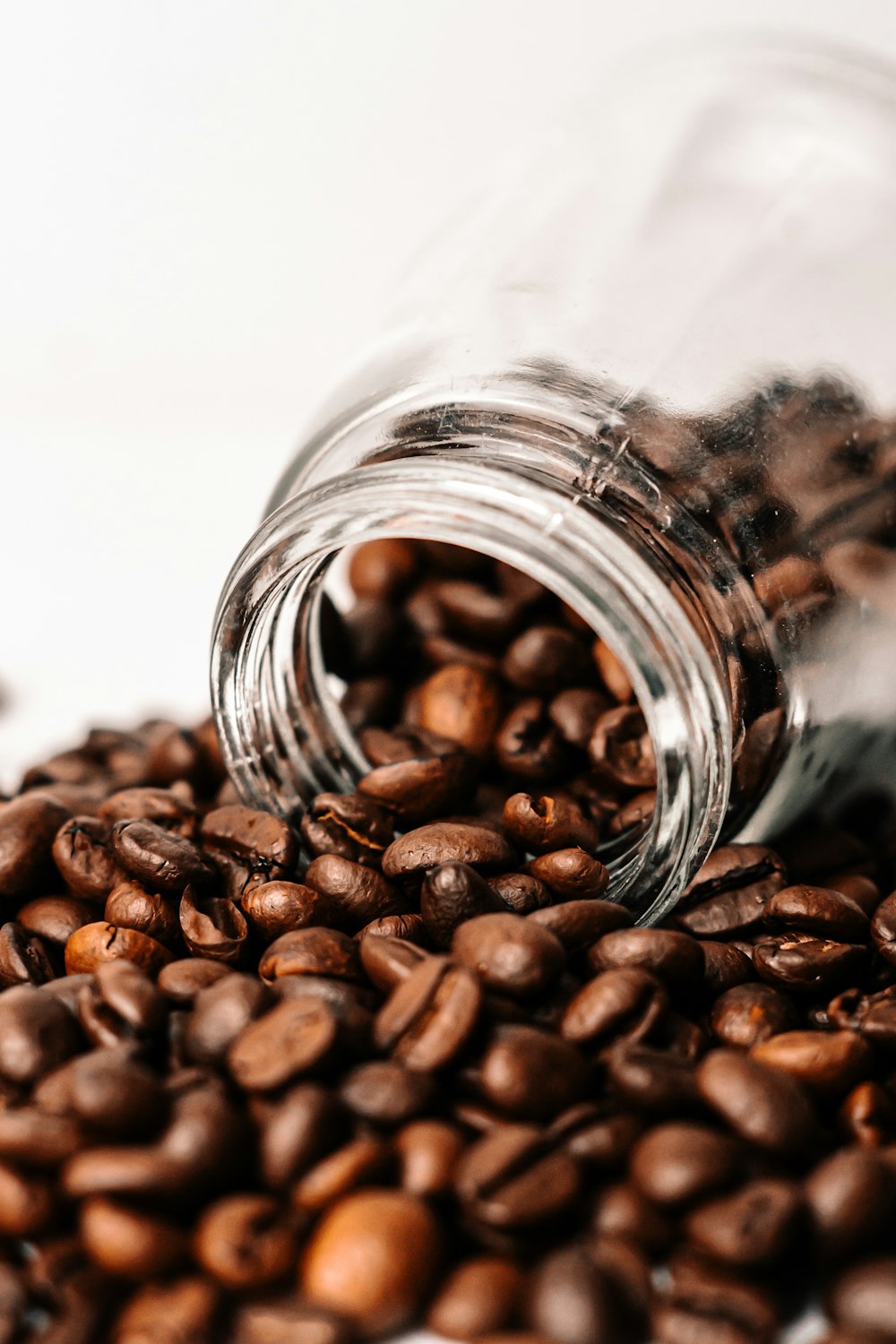 a glass jar filled with coffee beans sitting on top of a pile of coffee beans