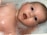A baby with wide eyes and an open mouth is lying in a bath filled with foam and bubbles. The baby's skin glistens with water, and the foam surrounds its head.