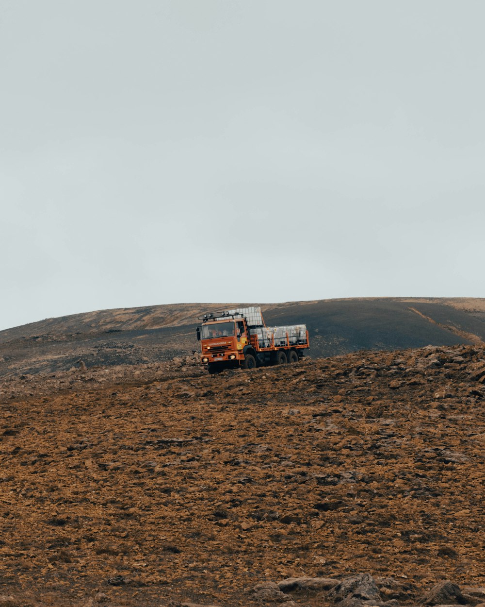 a truck driving down a dirt road next to a hill