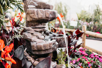 An elegant ceramic water fountain with a natural stone look, surrounded by green plants.