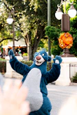 Bobo, the friendly blue bear, holding a bunch of colorful balloons in a park.