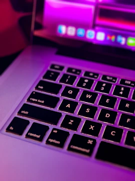 Close-up of a computer technician repairing a laptop with pink-themed website interface in the background