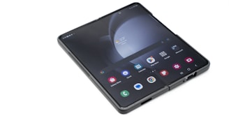 A modern foldable smartphone is displayed in its open configuration, showcasing its main screen with various apps and a weather widget. The screen is large and square, with a visible hinge in the middle.