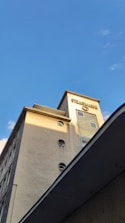 A tall building with a modern architectural design featuring circular windows and a light beige facade. The top of the building has a sign with the name 'STRASSMANN' in bold letters, and the structure is illuminated by sunlight against a clear blue sky.