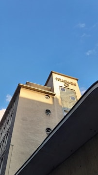 A tall building with a modern architectural design featuring circular windows and a light beige facade. The top of the building has a sign with the name 'STRASSMANN' in bold letters, and the structure is illuminated by sunlight against a clear blue sky.