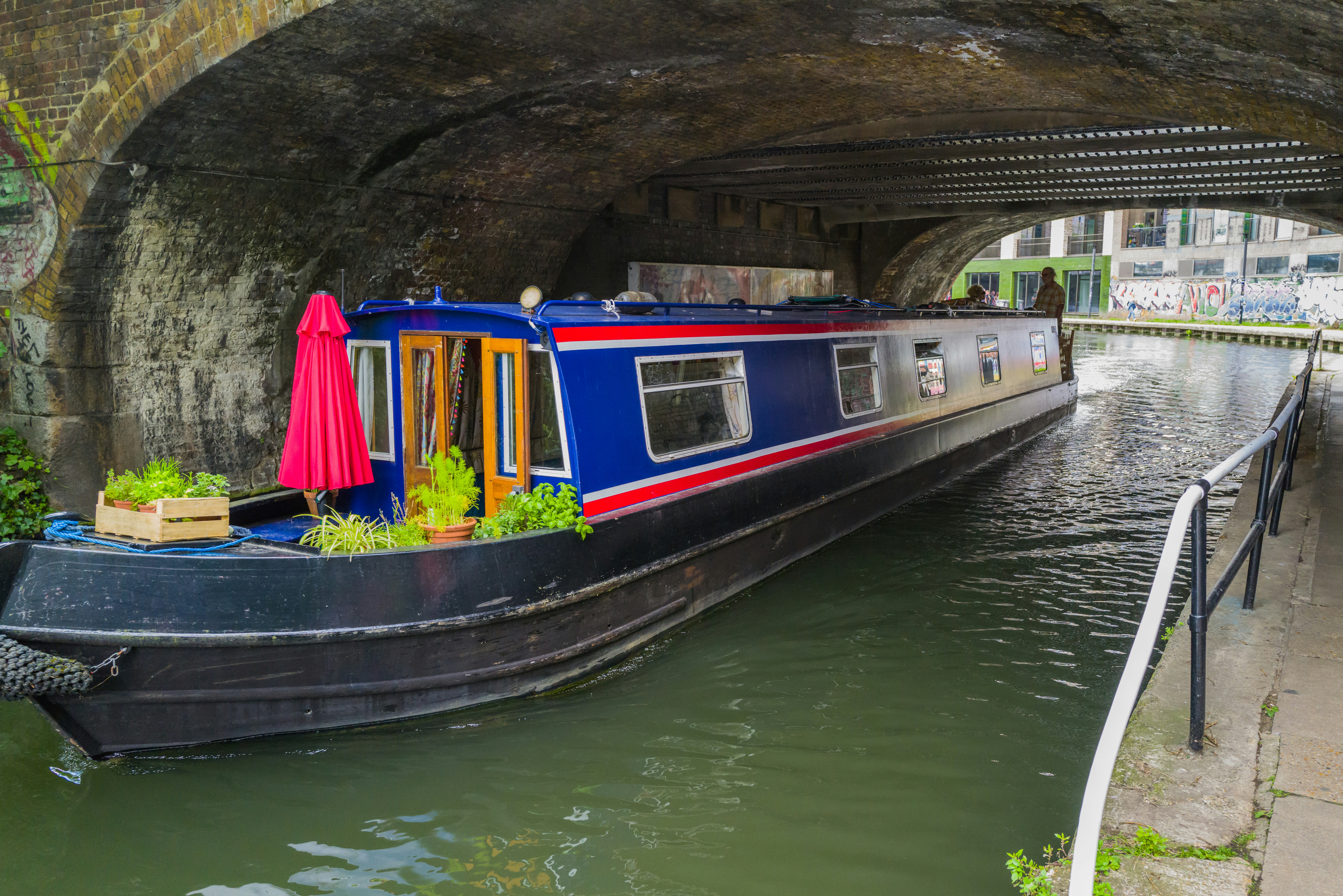 a boat with plants on the side of a river under a bridge