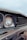 Close-up view of an old, rusty car front, focusing on a round, weathered headlight and a grille with visible corrosion. The paint appears faded, with noticeable rust spots along the edges.