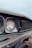 Close-up view of an old, rusty car front, focusing on a round, weathered headlight and a grille with visible corrosion. The paint appears faded, with noticeable rust spots along the edges.