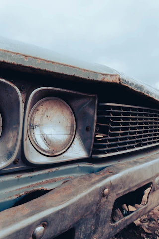 Close-up of the front grill of a rusty antique car caught in soft morning light.