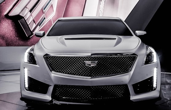 A sleek and modern car with a prominent front grille, angular headlights, and a smooth hood design. The car is set against a sophisticated backdrop that features geometric shapes and lines.