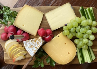 a wooden cutting board topped with cheese and fruit