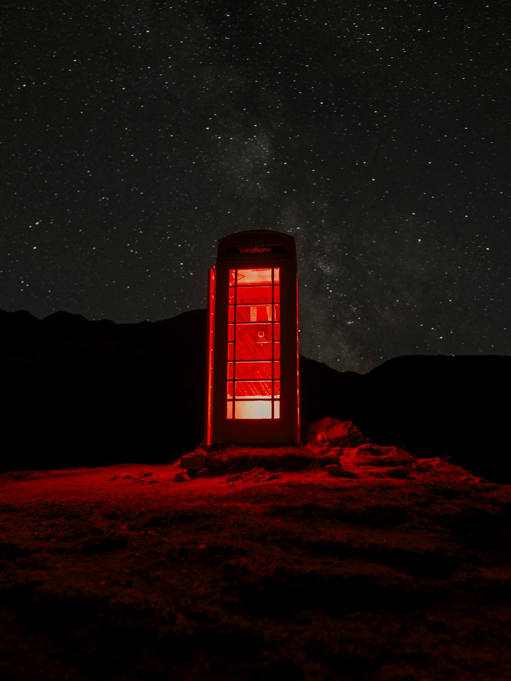 Una cabina telefonica rossa seduta sulla cima di una collina sotto un cielo notturno