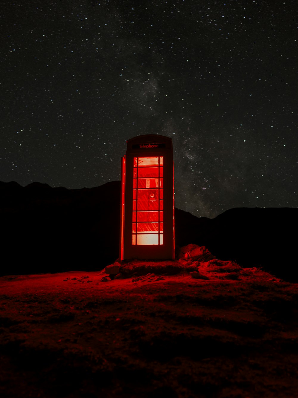 Eine rote Telefonzelle, die auf einem Hügel unter einem Nachthimmel sitzt