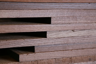 Close-up view of stacked wooden planks with visible grain patterns. The planks are neatly aligned, creating a layered texture.