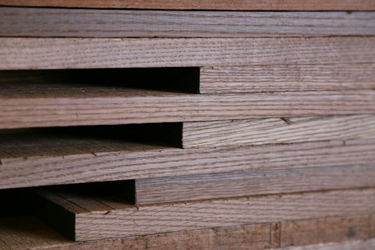 Close-up view of stacked wooden planks with visible grain patterns. The planks are neatly aligned, creating a layered texture.