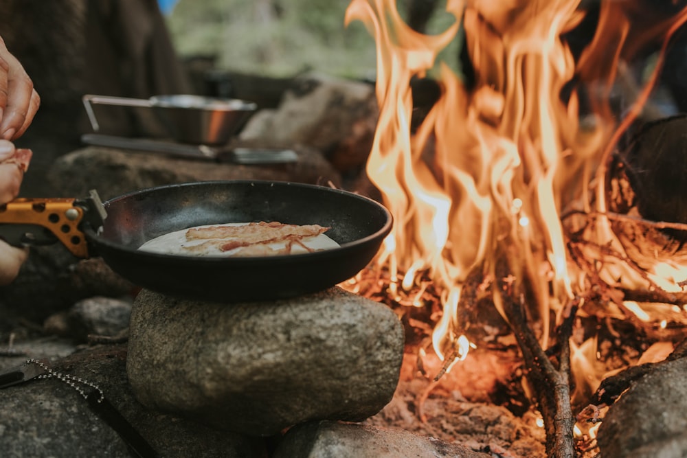 une personne qui fait cuire des aliments sur une poêle au-dessus d’un feu de camp