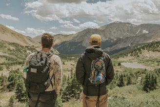 A pair of travelers with backpacks smiling in front of a scenic mountain view.