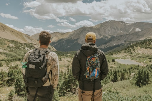 A pair of travelers with backpacks smiling in front of a scenic mountain view.