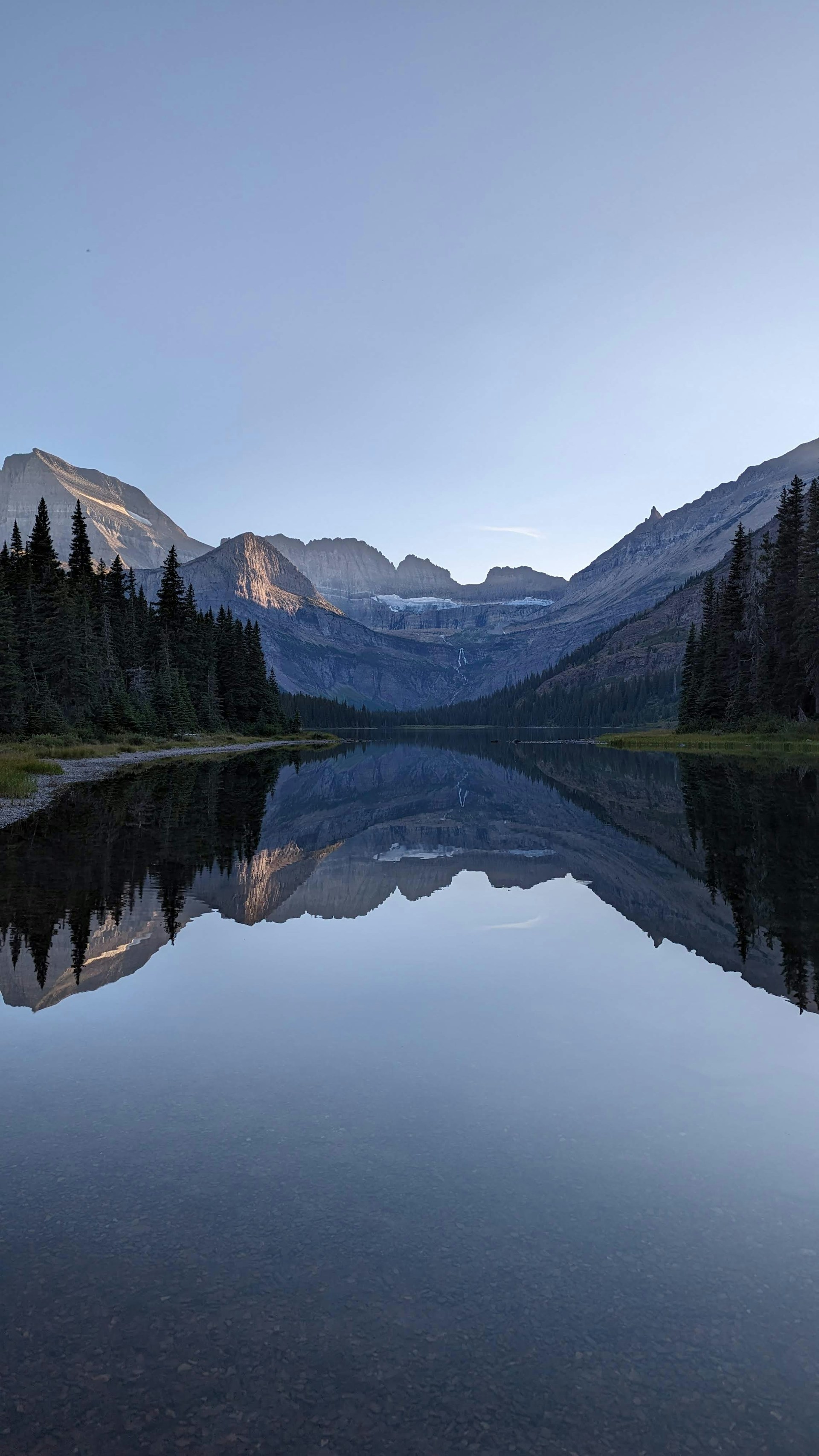 A tranquil mountain lake reflecting the clear blue sky and surrounding pine trees, inviting peaceful reflection.