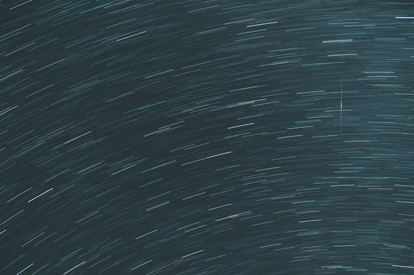 Long exposure photograph capturing star trails creating curved streaks across the night sky, giving a sense of motion and rotation.