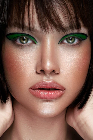 Close-up of a model wearing bold green eyeliner and soft pink lips, framed by wavy, abstract shapes.