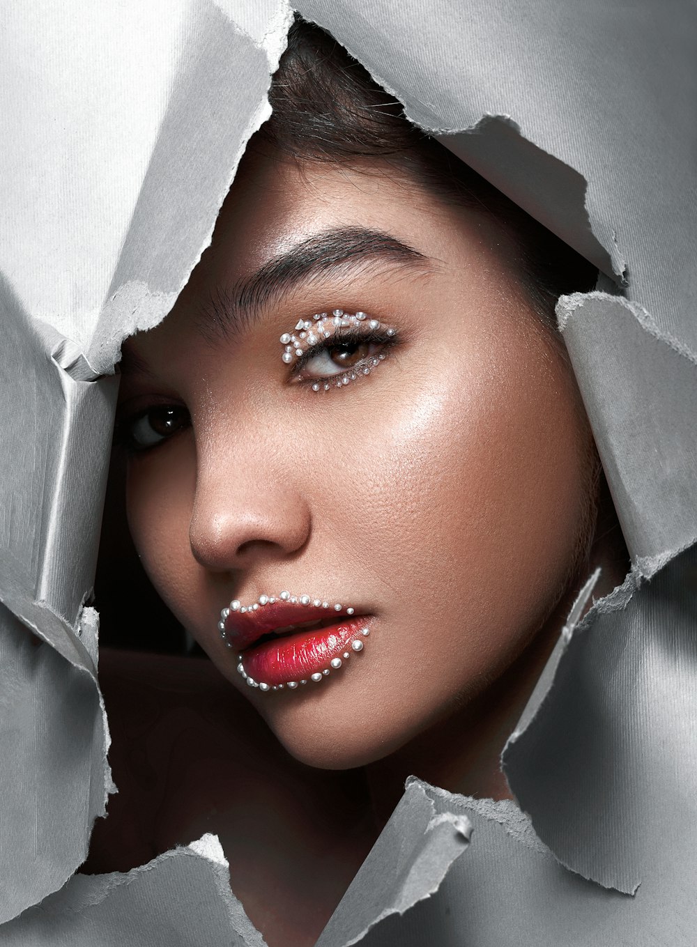 a woman with silver makeup is looking through a hole in a sheet of paper