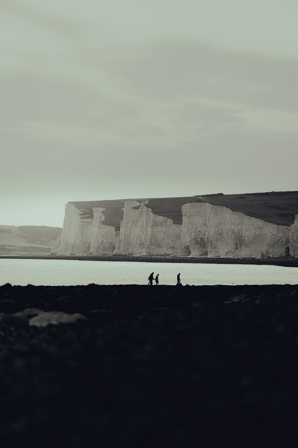 a black and white photo of people walking on a beach