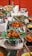 A vibrant display of various dishes served on banana leaves, arranged in metal trays and clay pots. The food includes fried and spicy items, with an assortment of accompaniments around. The setting appears to be a buffet or a festive food setup.