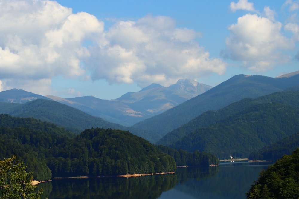 a lake surrounded by mountains under a cloudy blue sky