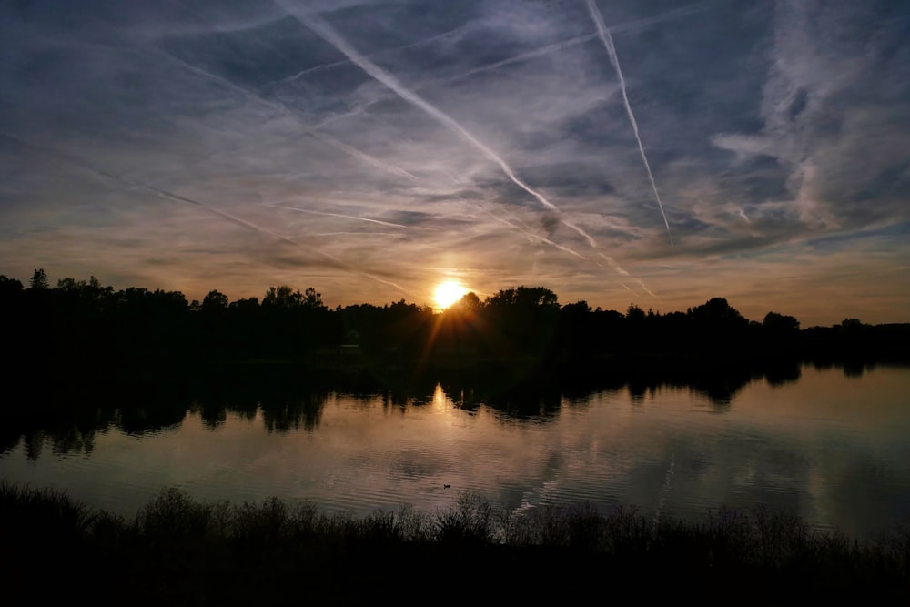 the sun is setting over a lake with contrails in the sky