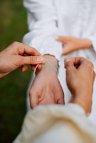 Hands fastening a delicate bracelet around another person's wrist. The background is softly blurred, emphasizing the interaction.