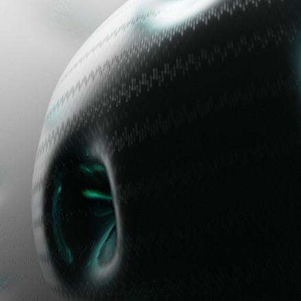 A dark, abstract image with a textured surface. The focus is on a rounded, oblong shape with some green highlights and a deep black area in the center, creating a mysterious and futuristic appearance. The background is a gradient mix of gray hues, adding to the overall enigmatic feel.