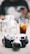 A classic Leica camera with a silver and black body is prominently placed on a table. In the background, there are blurred objects including glass bottles and a faint figure holding a phone. A glass with a drink, possibly iced tea, is also visible nearby.