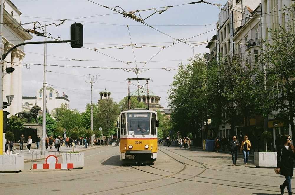 a yellow and white train traveling down a street next to tall buildings