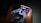 A person is holding a small electronic device, possibly a smartphone with a foldable screen, playing a video game. The game features a dark, fiery theme with icons or characters displayed on the screen.