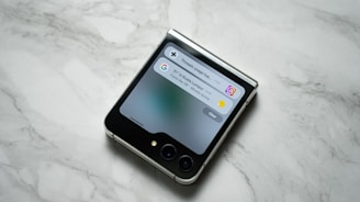 A flip smartphone is placed on a marble surface, displaying notifications on its cover screen.