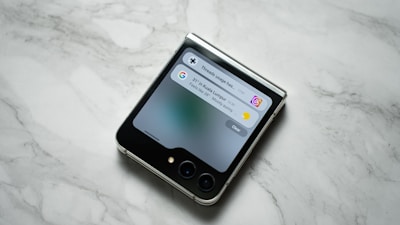 A flip smartphone is placed on a marble surface, displaying notifications on its cover screen.