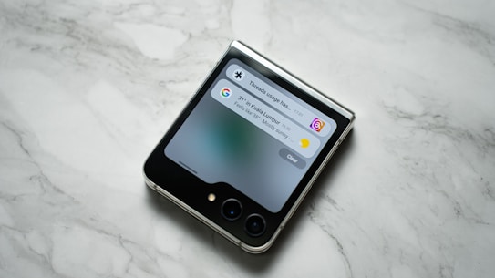 A flip smartphone is placed on a marble surface, displaying notifications on its cover screen.