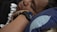 A person is lying down with their head resting on a pillow, wearing a smartwatch on their wrist. The pillow has a dark blue pattern with white accents.