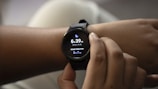 A person is adjusting a smartwatch on their wrist with their other hand. The smartwatch screen displays the current time, sleep duration, and includes a moon icon, possibly indicating sleep tracking.