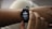 A person is adjusting a smartwatch on their wrist with their other hand. The smartwatch screen displays the current time, sleep duration, and includes a moon icon, possibly indicating sleep tracking.